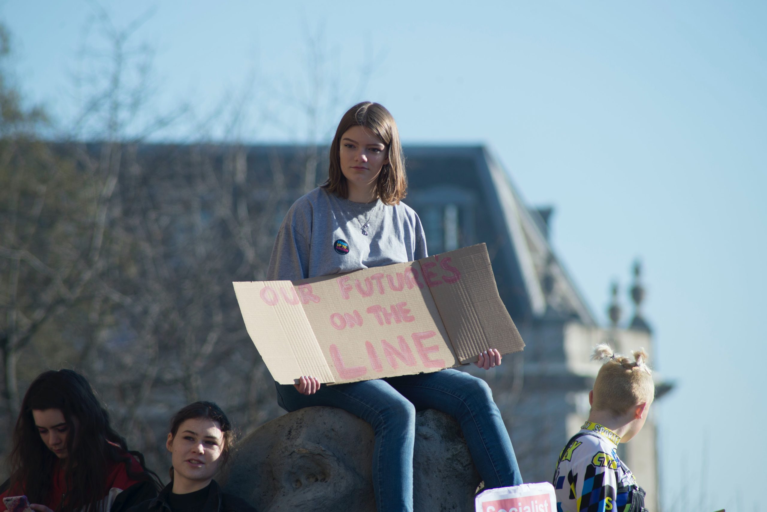 Teen girl attends environmental protest and holds sign reading Our Future's on the Line