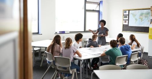 Photo of Female High School Tutor Standing By Table With Students Teaching Lesson